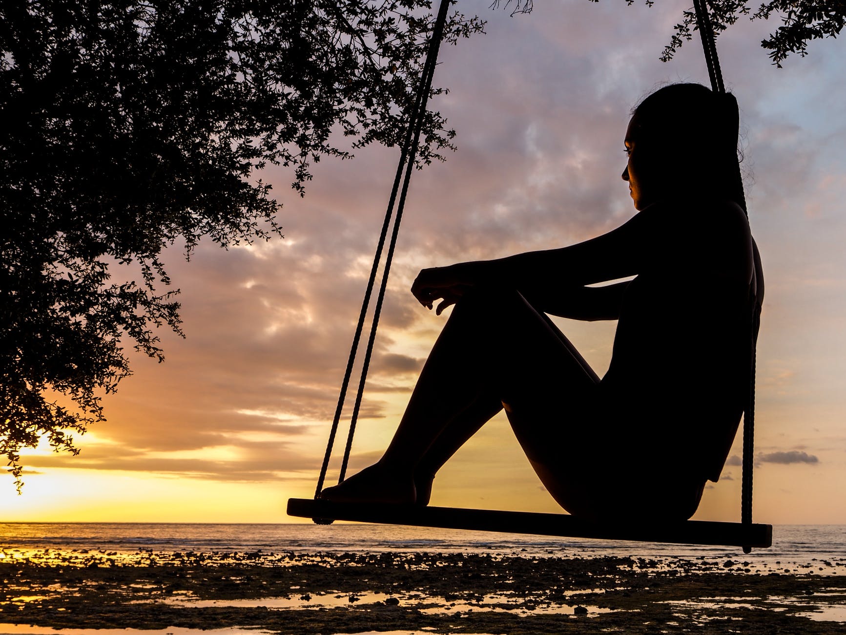 A serene sunset silhouette of a woman sitting on a swing by the seashore