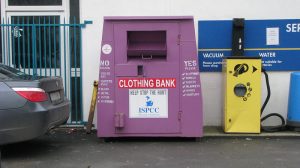 A purple clothing bank placed near a parked car.