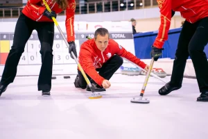 A man crouched down and playing curling with his teammates.