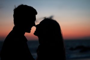 Silhouette of a man and woman about to kiss during a sunset.