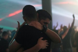 Two men hugging each other inside a nightclub.
