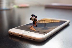 A miniature person skateboarding into a cellphone.