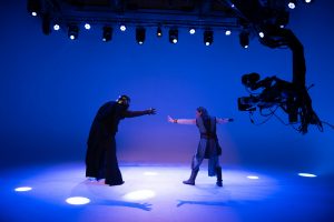 Actors in Star Wars costumes performing in front of a camera on a blue-lit stage.