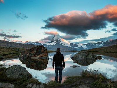 A man standing on a rocky cliff facing a body of water.