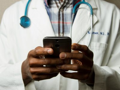A doctor with a teal stethoscope using a phone.