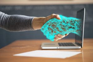 A person shaking hands with a technological hand coming from a laptop.