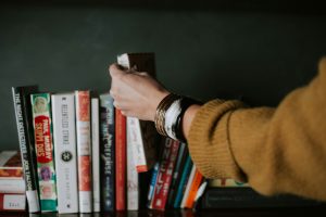 Person picking white and red book from a bookshelf.