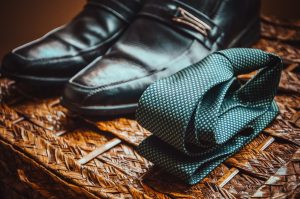 A grey necktie folded beside a pair of dress shoes.