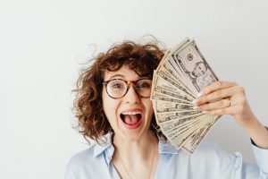 A smiling woman in a blue long-sleeved blouse holding dollar bills.