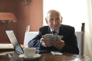 A senior businessman holding money in his hands while seated at a table.
