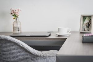 A workspace with a laptop, cup, and a framed picture of a woman.