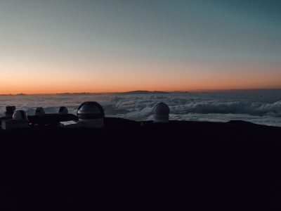 Silhouetted observatories atop Mauna Kea with a dramatic sunset over the clouds.
