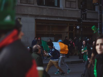 A vibrant street celebration in Chicago with people waving an Irish flag during the day.