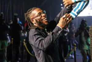 Burna Boy pictured smiling and shaking hands with another person.