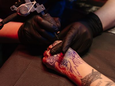 A tattoo artist wearing black gloves working on a detailed dragon design in a studio.