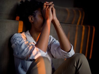 A woman sitting against the sofa with her hands against her forehead.