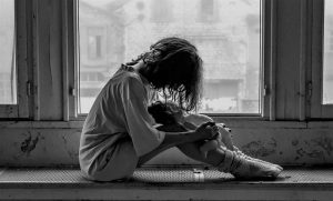 A greyscale image of a woman sitting by the window.