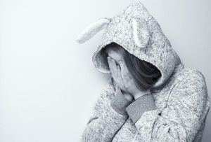 A greyscale image of a woman in a hoodie covering her face.