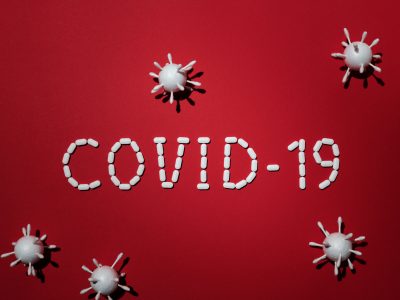 Artistic representation of COVID-19 using pills and virus models on red background.
