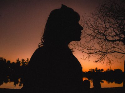 A silhouette of a woman by a lake at sunset, surrounded by trees and a vibrant orange sunset sky.