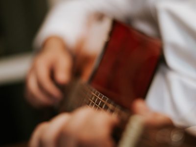 Blurred close-up of a person playing an acoustic guitar indoors.