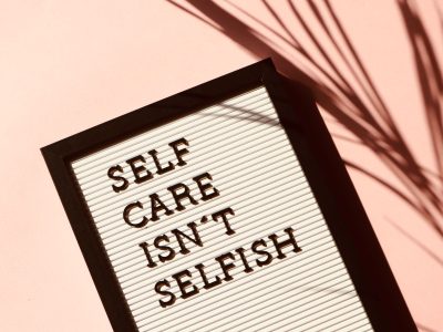 Letter board displaying 'Self Care Isn't Selfish' with artistic shadow on pink background.