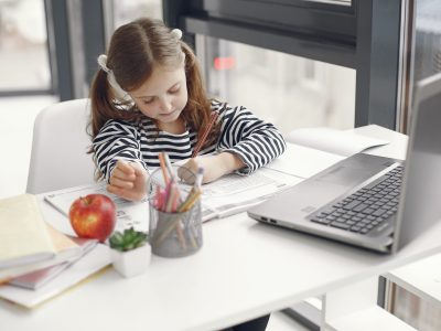 A young girl studies at home using a laptop, engaged with her homework and school supplies.