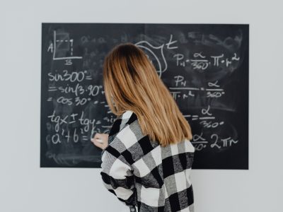 Teenager writing mathematical formulas on a blackboard in a classroom setting.
