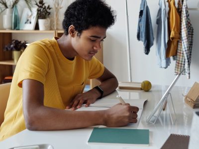 Focused teen studying indoors with a tablet and notebook at home.