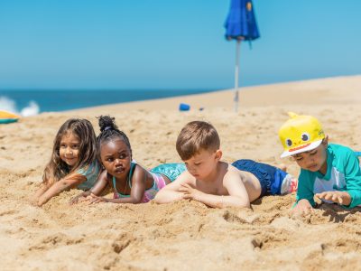 A diverse group of kids playing together on a sandy beach under the sun.