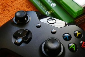 A photo of an Xbox One controller next to a stack of three video games. 