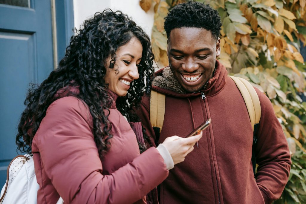 A man and a woman smile while looking at a cell phone screen.