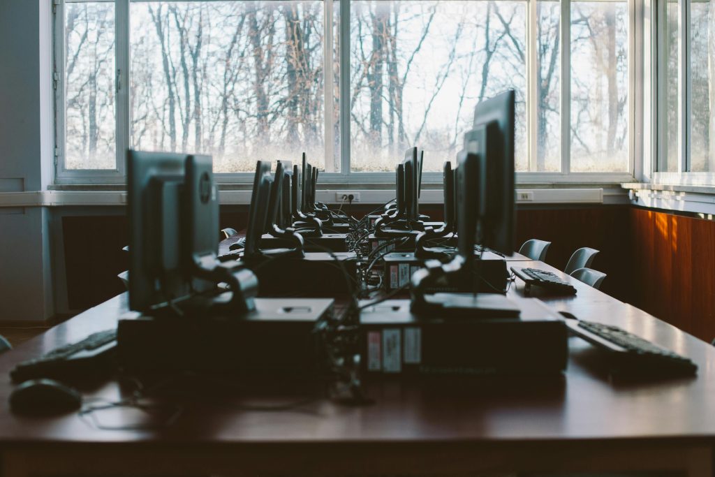 A table of desktop computers by a window. 