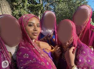 Five east African girls wearing pink Ethiopian cultural clothes looking at the camera. Four of the girls are blurred out and one of them is not.