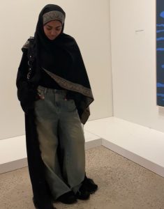 Young girl wearing long black hijab and a black abaya with blue jeans.