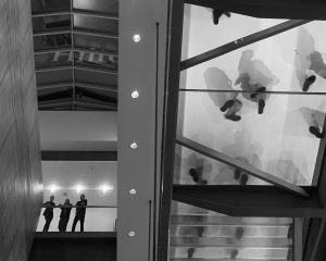 Silhouettes of people standing above on a glass-floor mezzanine