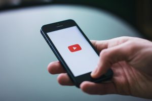 Close-up photo of someone holding a phone with the YouTube logo on screen.