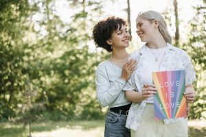 Two women in love, holding a rainbow "Love is Love" sign.