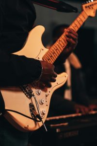 A Black man plays a white electric guitar