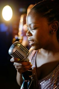 A Black woman sings into a handheld microphone with her eyes closed