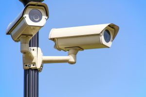 Two CCTV cameras attached to a pole, against a blue sky.