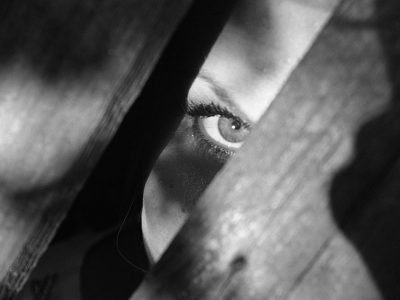 A person looks through a gap between two pieces of wood. Photo is in black and white.