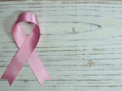 A folded pink ribbon symbolizing breast cancer awareness on a grey, wood grain background.