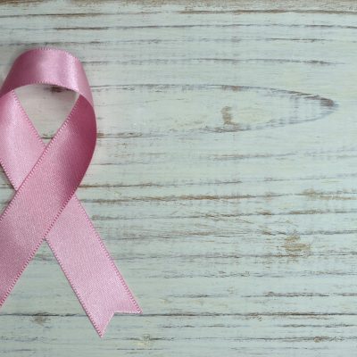 A folded pink ribbon symbolizing breast cancer awareness on a grey, wood grain background.