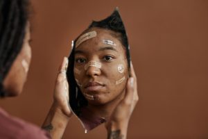 Woman looking in the mirror to see herself with bandaids on her face with words written of her imperfections.