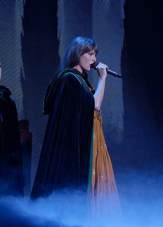 Photo of Taylor Swift singing on stage wearing a dark cloak.