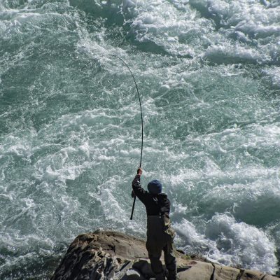 Person fishing from a rock in rapidly flowing water