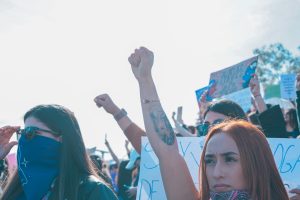 A photo of protesters wearing face masks and holding their fists in the air at a rally