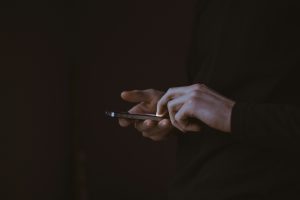 A photo of white hands holding a cell phone against a black bakground