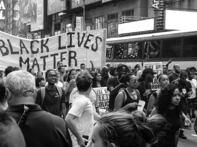 A black and white photo of a Black Lives Matter rally, featuring a large "Black Lives Matter" banner